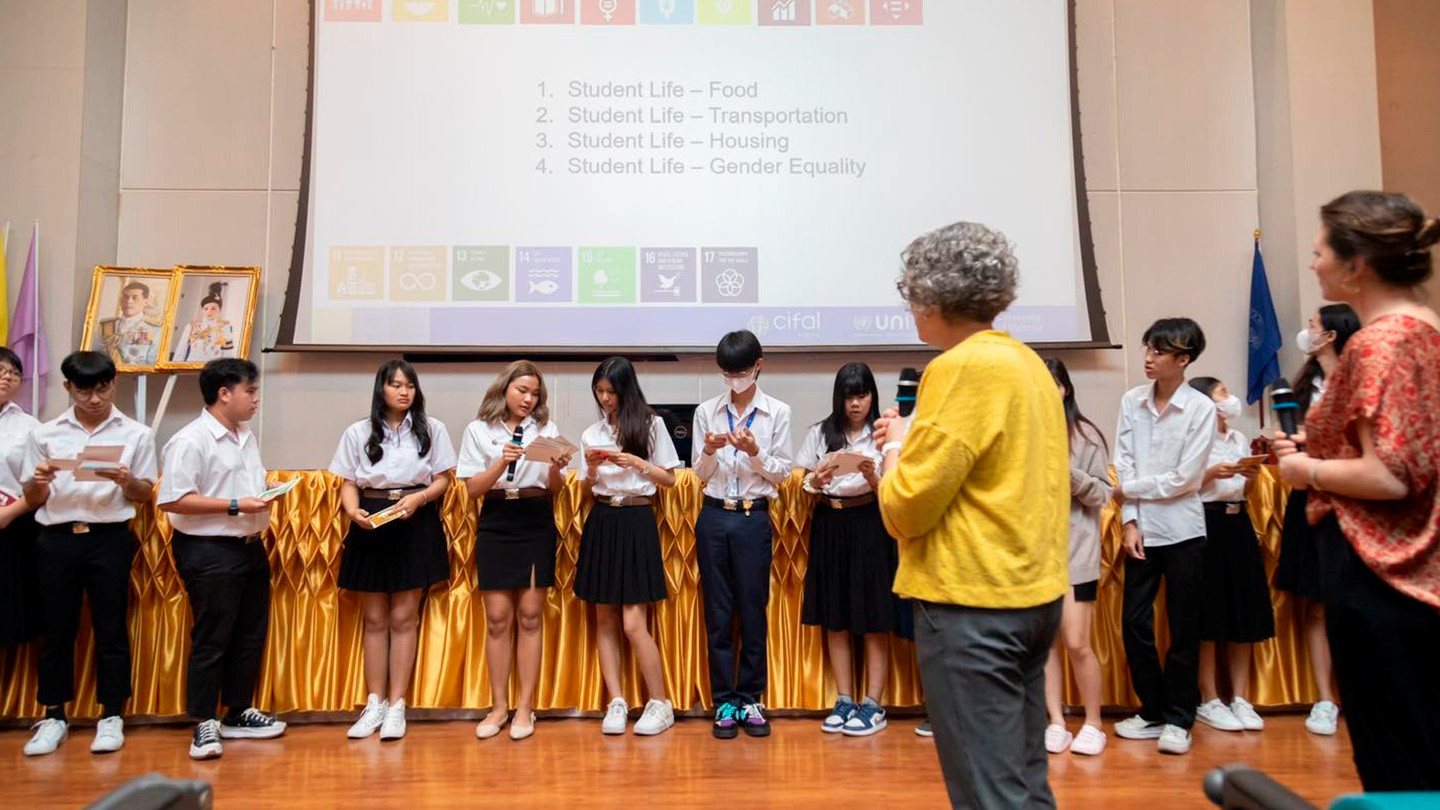 Professor Heather Ranson teaching students in Thailand about SDGs. She is standing on stage with the students as they present their ideas and discuss SDGs.