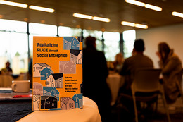 Book "Revitalizing PLACE through Social Enterprise" on a table with people in the background