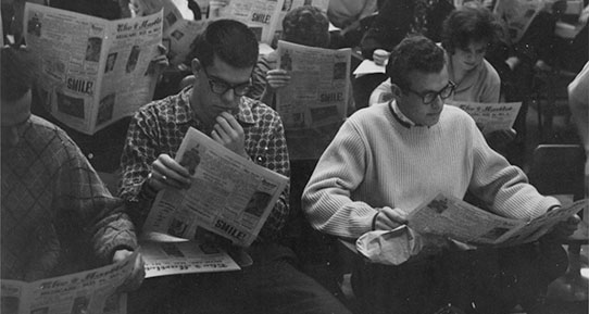 Students sitting in a lecture theatre reading the Martlet newspaper.
