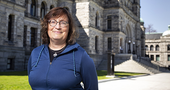 A photo of a woman in a blue hoodie standing in front of a large stone building.