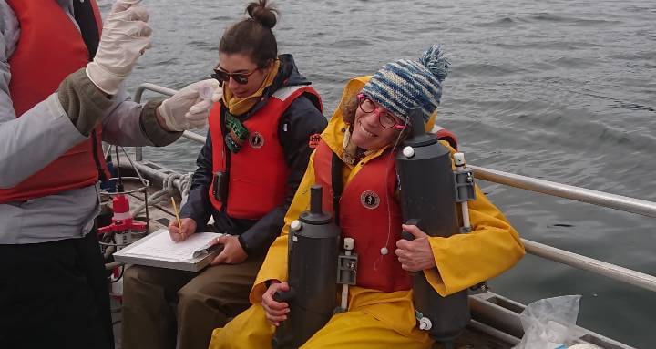 Roberta Hamme in a yellow rainsuit, toque and life jacket on a bot, holding two cylinders