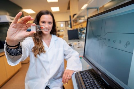 Elvira seated in her lab, holding up a microfluidic chip
