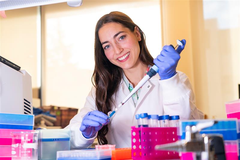 Shaeleen Mihalynuk in a lab coat and gloves pipetting a sample.