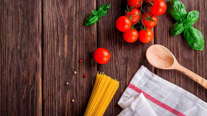 Spaghetti noodles, fresh tomatoes and basil on a wooden table.