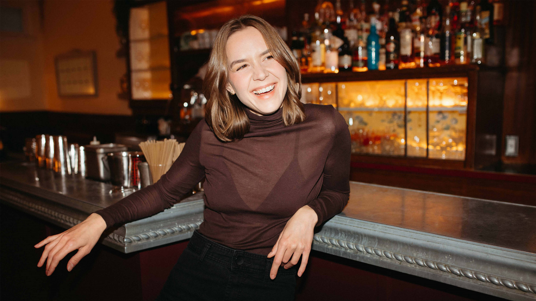 Woman smiling while leaning against a bar. 