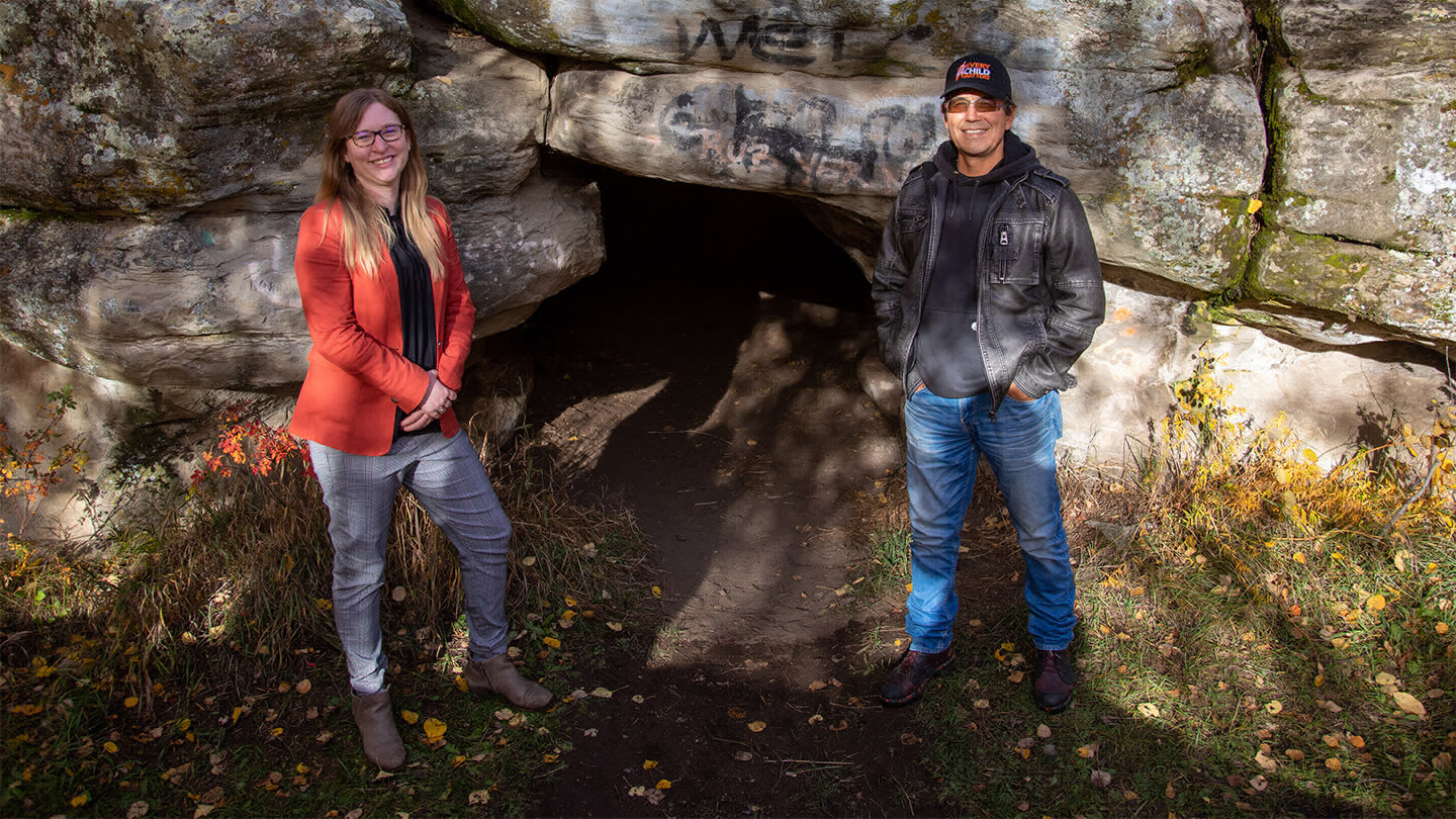 Woman and man standing beside the entrance to a cave.