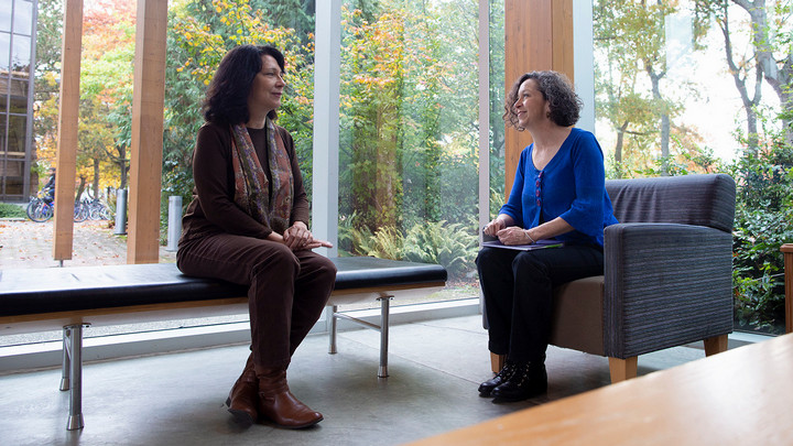 Two women sit talking inside a building at UVic.