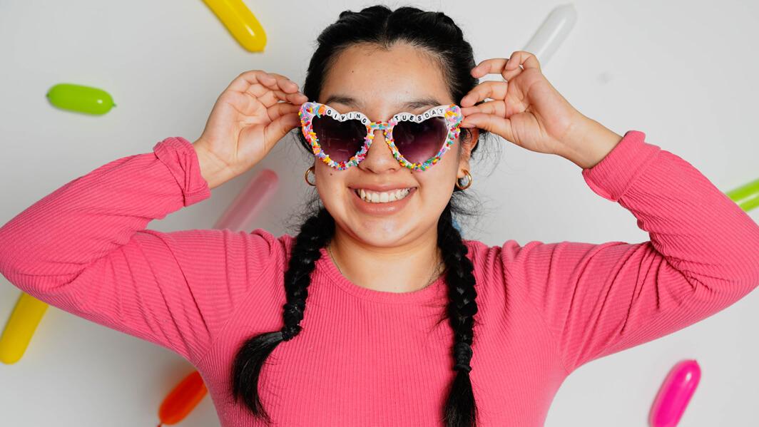 A young woman in pink with heart-shaped sunglasses lined with sprinkles.