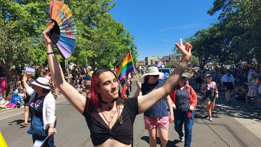Person in front of a large group with a rainbow fan at a Pride parade.