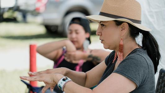 A woman with dark hair holds out her hands while teaching Cree language.