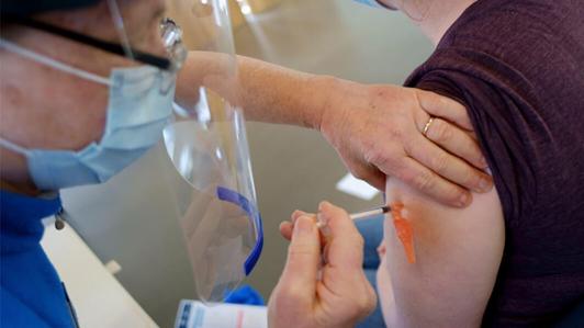 A health care worker administers an injecting into a patient's upper arm.
