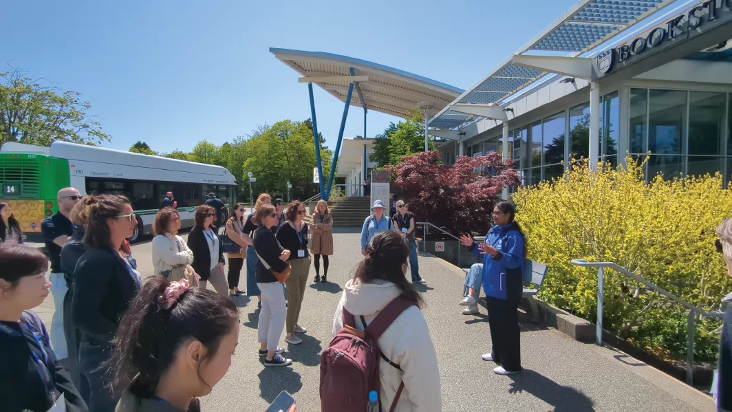 Group of visitors having a campus tour outside the UVic bookshop in a sunny day