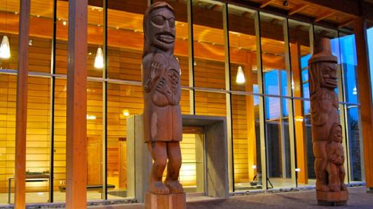 Photo of the entrance of the First Peoples House at UVic, featuring the two poles carved by Tsawout artist Doug LaFortune