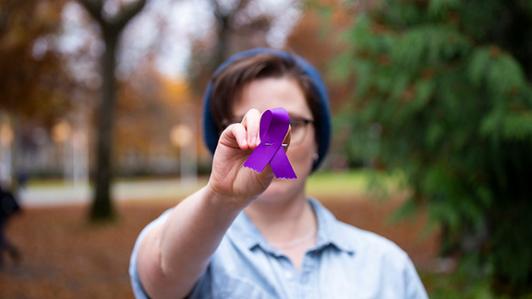 Photo of a person holding a purple ribbon towards the camera 