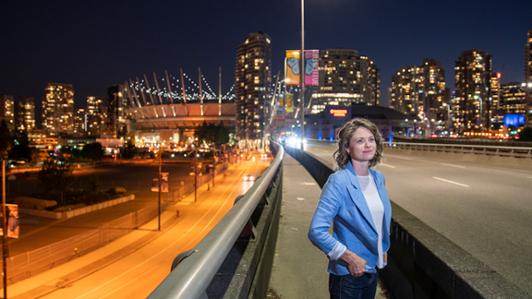 Photo of Civil engineer Madeleine McPherson standing on a bridge in Vancouver at night, with the illuminated city in the background