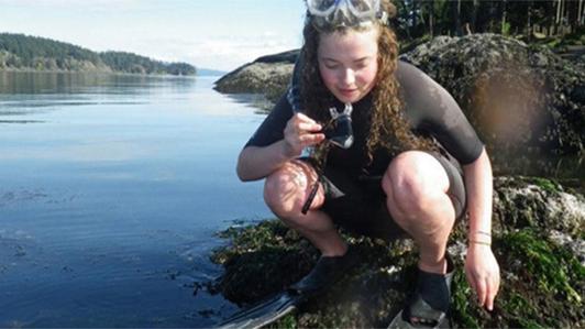 Young female with diving gear (fins, googles and wetsuit) on a rock and and looking down to the ocean at the Bamfield Marine Science Centre on Vancouver Island