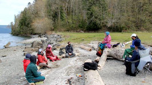 Photo of Cowichan Tribes Research Director Dianne Hinkley on the beach at Tl’ulpalus in Cowichan Bay sharing with students stories of the clash between colonial land law and Indigenous land rights 