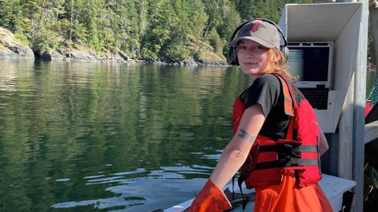UVic co-operative education student stands on a boat, with an island of trees in the background.