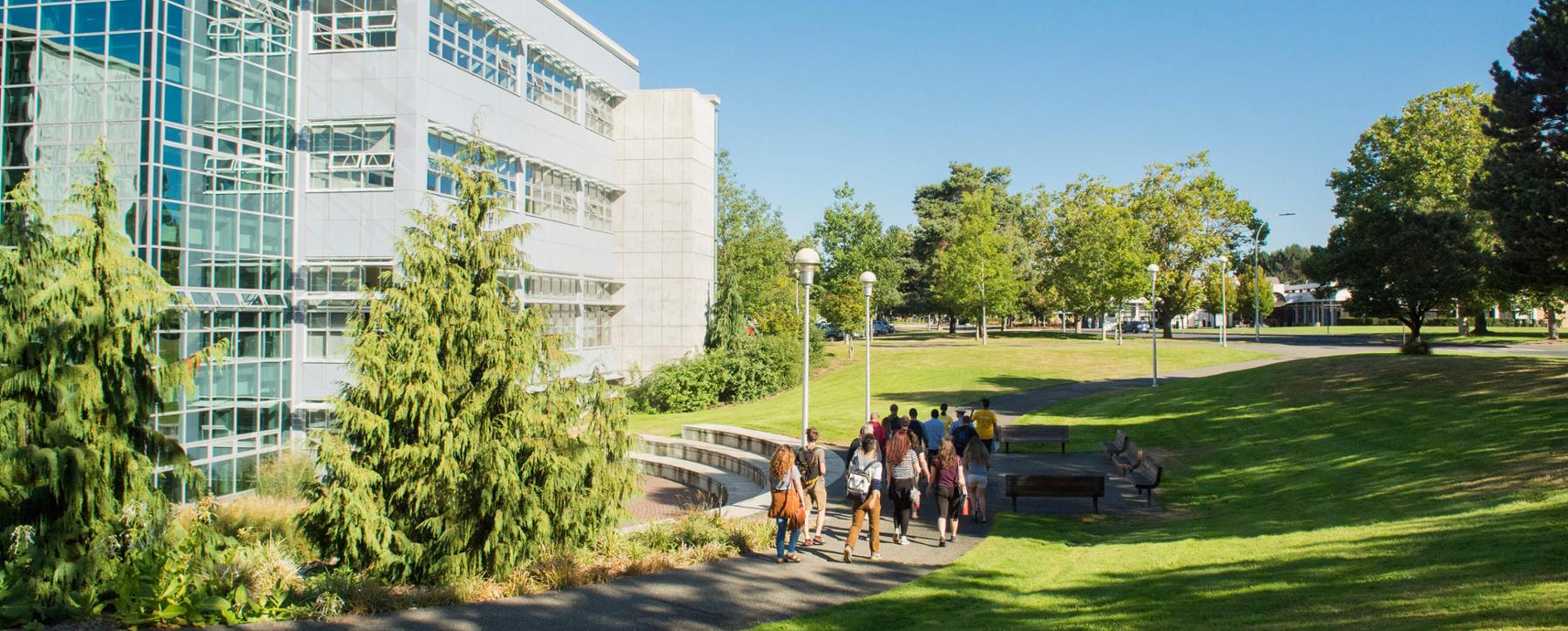 A group of people walk along a campus pathway next to the Engineering and Computer Science building at UVic