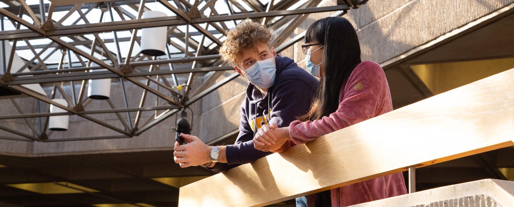 Two masked students stand on the upper mezzanine of the Jamie Cassels Centre at UVic.
