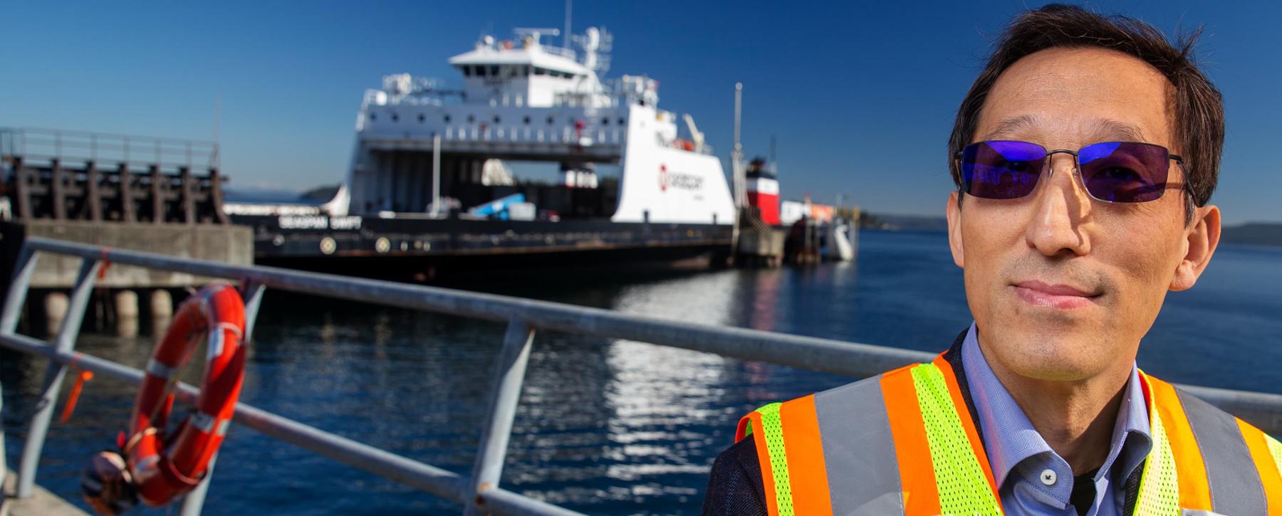 researcher with ocean and ferry behind