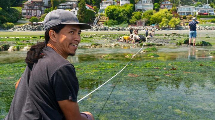 An Indigenous man turns to the camera and smiles during a field school trip to Cordova Bay.