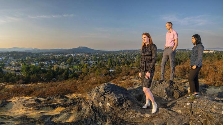 Three people stand on top of a mountain at dusk gazing at the scenery.
