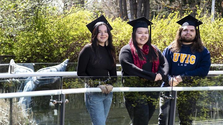 Three Indigenous alumni stand in front of a foundtain at UVic campus.