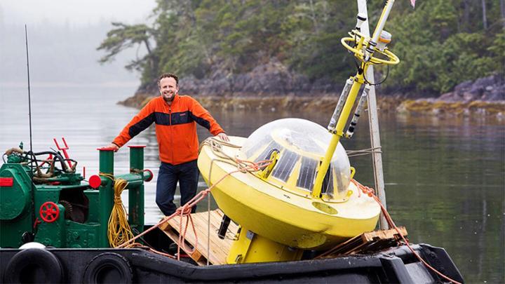 Brad Buckham (with a wave measurement buoy) in front of the Hesquiaht First Nation community of Hot Springs Cove.