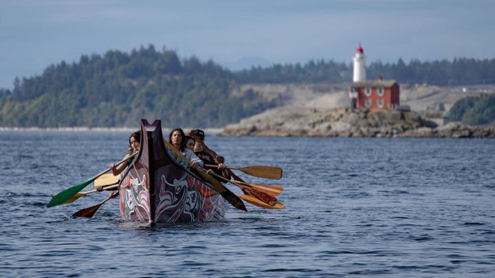 Young Indigenous people row a canoe in the ocean.