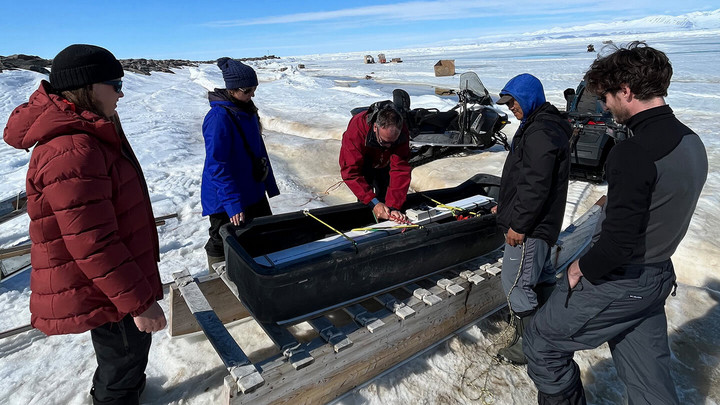 Five people in Arctic gear load an electromagnetic ice profiler into the qamutik.