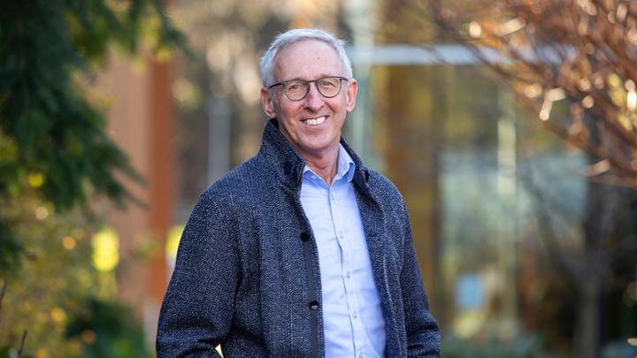 President Kevin Hall standing outside in a blue jacket. The background is blurred and Hall is smiling