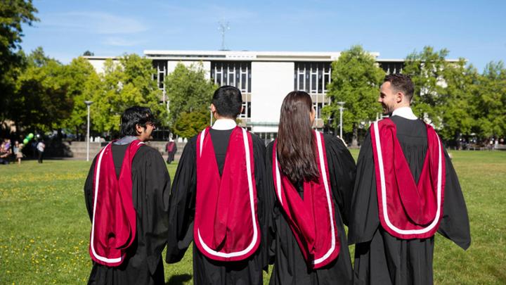 Four graduating studens walk across the campus quad.