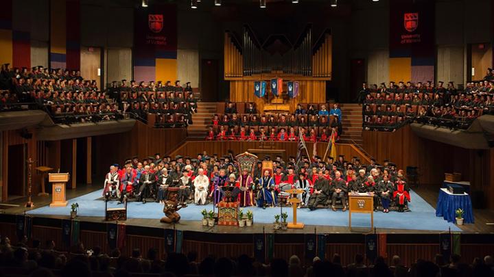 The stage at Farquar arraged for convocation. Chancellor Rogers sits at the centre dias, surrounded by UVic faculty and administrators. Graduating students site in rows of seats above the stage.