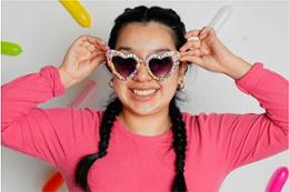 A young woman in pink with heart-shaped sunglasses lined with sprinkles.