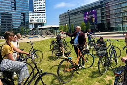 A group of people gather together in a grassy park area and stand with or on bicycles.