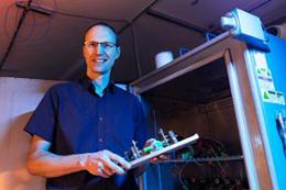 Curran Crawford smiles at the camera holding a piece of machinery.
