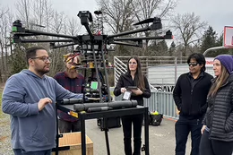 Five people stand together as they review a drone's settings before a test flight.