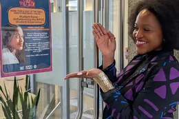 A smiling student gestures toward a poster featuring a talk that she is hosting.