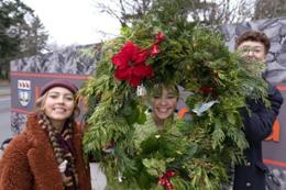 Three students holding holiday wreath