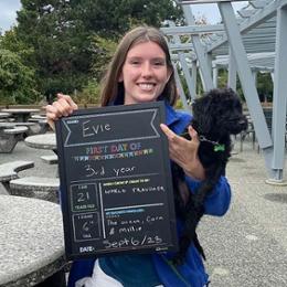 Sitting student holding small black dog and "first day of" back to school sign.
