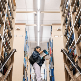 Student reading a book in between library aisles.