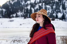 An Indigenous woman stands outside with a snowy landscape behind her and smiles with her eyes closed.