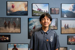 Co-op student Jay Choi standing in front of a wall of pictures depicting a wild fire fighter actively engage in wild fire events