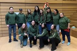 Kali poses with a group of students all wearing dark green Campus Cousin hoodies.