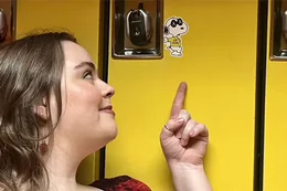 A student points at a Snoopy sticker on a bright yellow locker.
