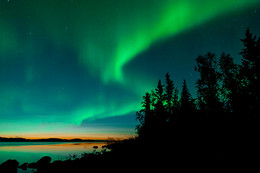 A landscape image of northern lights in the night sky along the coastline.