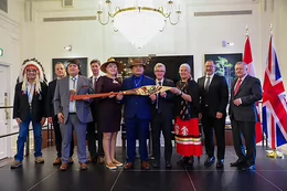 A group of people stand together as several hold a paddle painted with Indigenous artwork.
