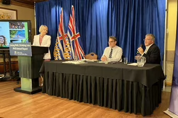 Dr. Bonnie Henry stands at a podium while Dr. Martin Lavoie sits with Tim Naimi at a panel discussion.