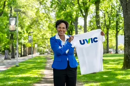 Dr. Rhonda McEwen stands on campus holding up a UVic t-shirt.